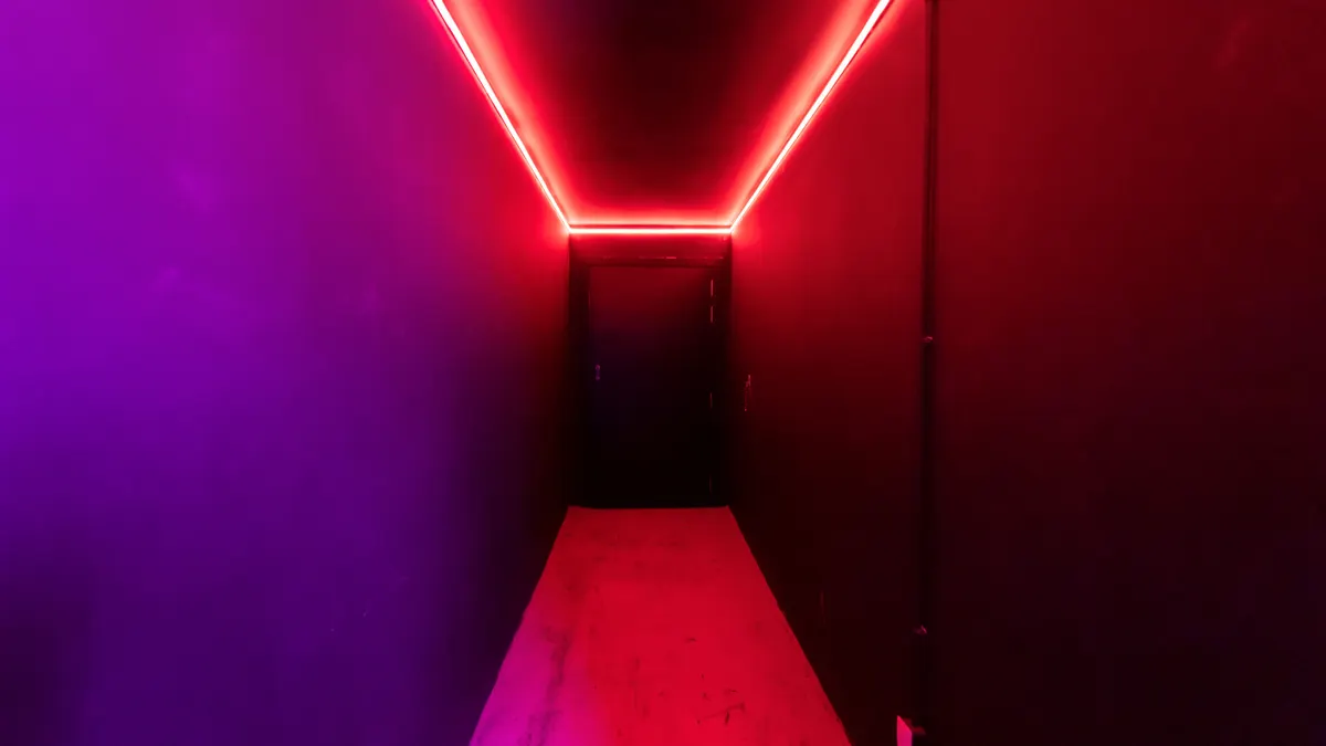 Un couloir éclairé au néon avec un mélange de lumières rouges et violettes dans une pièce sombre.